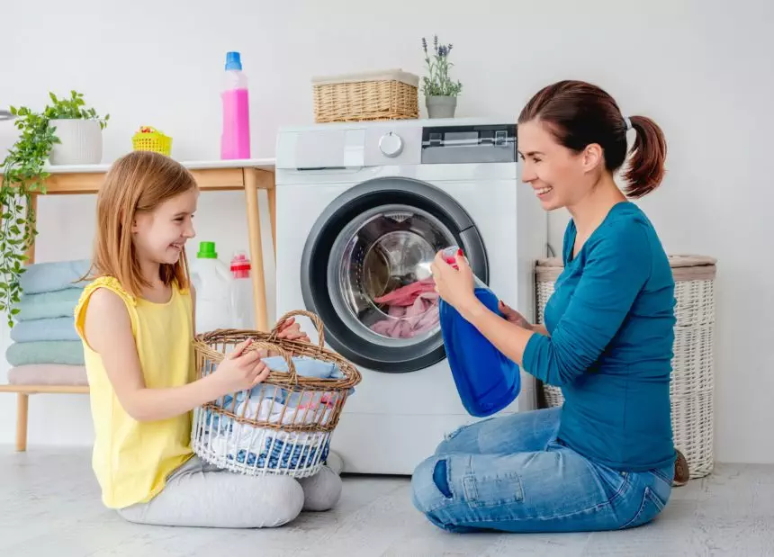 Happy mother and little daughter washing clothes